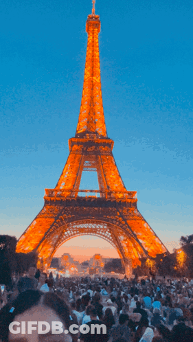 A Crowd Of People Are Gathered In Front Of The Eiffel Tower At Night GIF