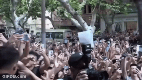A Crowd Of People Are Holding Their Phones Up In The Air While A Man Takes A Picture Of Them . GIF