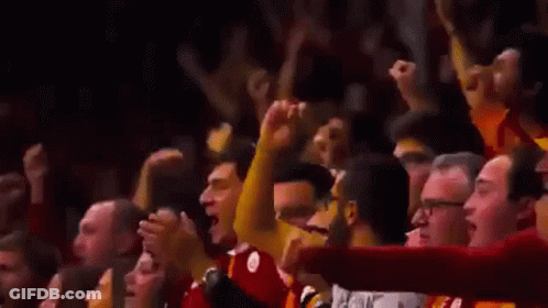 A Crowd Of People Are Raising Their Arms In The Air At A Basketball Game . GIF