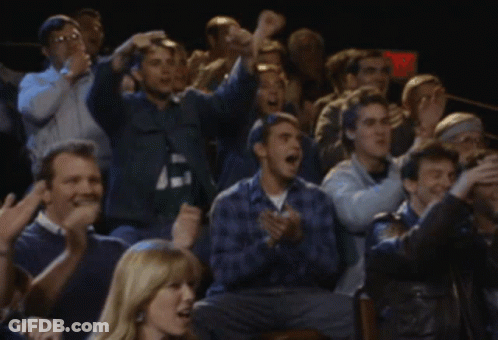 A Crowd Of People Are Sitting In A Dark Room With A Red Exit Sign In The Background GIF