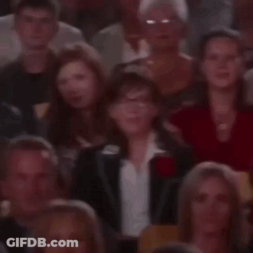 A Crowd Of People Are Sitting In A Stadium Watching A Show And One Woman Is Smiling . GIF