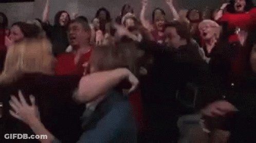 A Crowd Of People Are Standing In A Room With Their Arms In The Air And Screaming . GIF