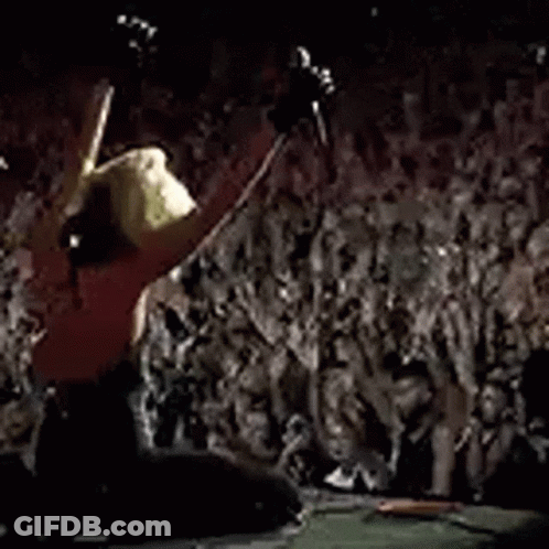 A Crowd Of People Are Standing In Front Of A Stage Watching A Concert . GIF
