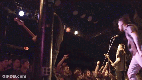 A Crowd Of People Are Watching A Band Perform On Stage With An Exit Sign In The Background GIF