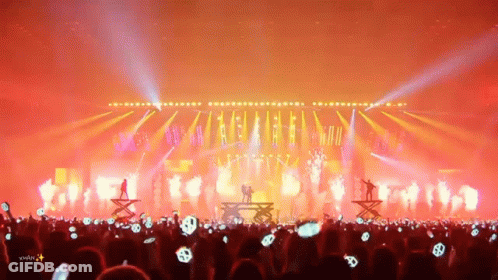 A Crowd Of People Are Watching A Concert With A Silhouette Of A Couple On Stage GIF