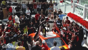 A Crowd Of People Gathered Around A Race Car GIF