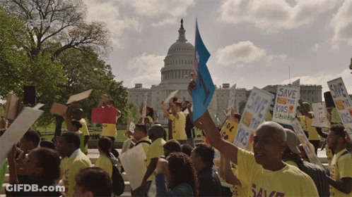 A Crowd Of People Holding Signs Including One That Says Save The Kids GIF