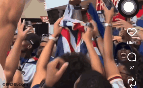 A Crowd Of People Holding Up A Flag With A Cbs Logo In The Background GIF