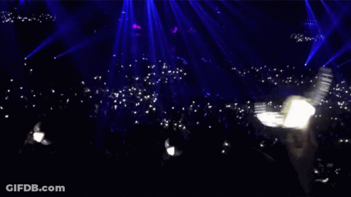 A Crowd Of People In A Dark Room With A Blue Light Behind Them GIF