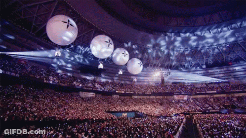 A Crowd Of People In A Stadium With Balloons Hanging From The Ceiling That Have A Cross On Them GIF
