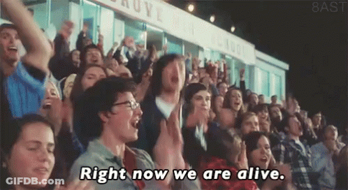 A Crowd Of People In A Stadium With The Words Right Now We Are Alive Written On The Screen GIF