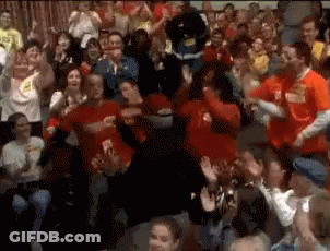 A Crowd Of People In Red Shirts Are Dancing And Clapping GIF