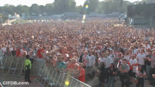 A Crowd Of People Standing In Front Of A Fence At A Festival GIF