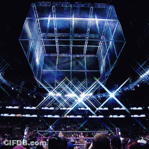 A Crowd Of People Watching A Wrestling Match In A Stadium With A Giant Cube In The Background GIF