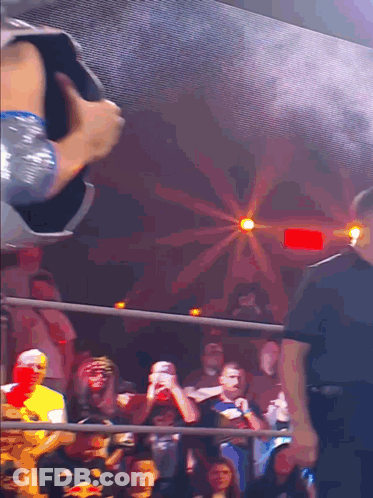 A Crowd Of People Watching A Wrestling Match With A Red Light Behind Them GIF