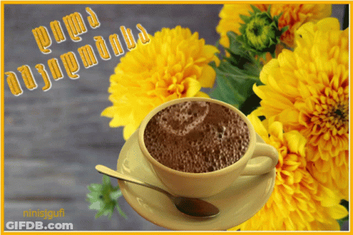 A Cup Of Coffee Sits On A Saucer With Yellow Flowers In The Background And A Greeting In A Foreign Language GIF