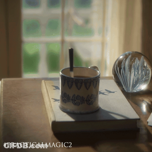 A Cup Of Coffee Sits On Top Of A Book Called Practical Magic GIF