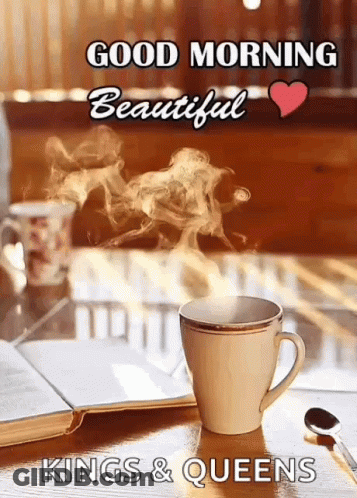 A Cup Of Coffee With Steam Coming Out Of It Is On A Table With A Book And A Spoon . GIF