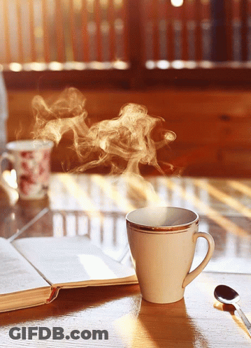 A Cup Of Coffee With Steam Coming Out Of It Sits On A Table Next To An Open Book GIF