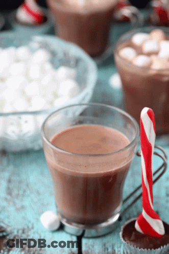 A Cup Of Hot Chocolate Next To A Candy Cane On A Table GIF