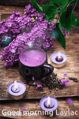 A Cup Of Purple Tea Surrounded By Purple Flowers And Candles On A Wooden Table . GIF