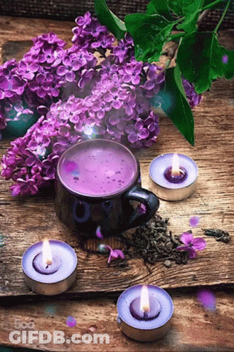 A Cup Of Purple Tea Surrounded By Purple Flowers And Lit Candles GIF