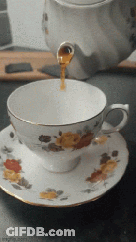 A Cup Of Tea Is Being Poured Into A Saucer With Flowers On It GIF