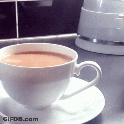 A Cup Of Tea Sits On A Saucer Next To A White Kettle GIF