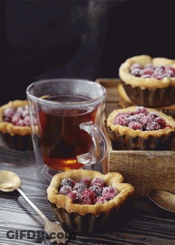 A Cup Of Tea Sits On A Table Next To A Tray Of Muffins GIF