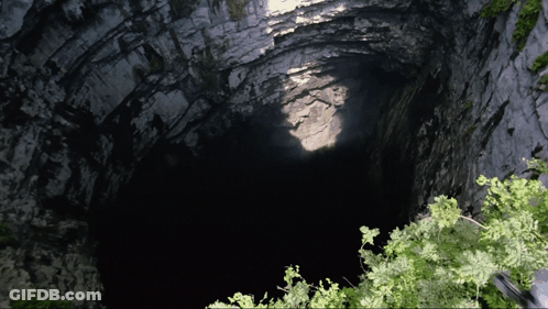 A Dark Cave With A Light Coming Out Of The Ceiling GIF
