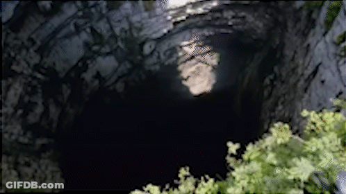 A Dark Cave With A Tree In The Foreground And A Light Coming Out Of It GIF