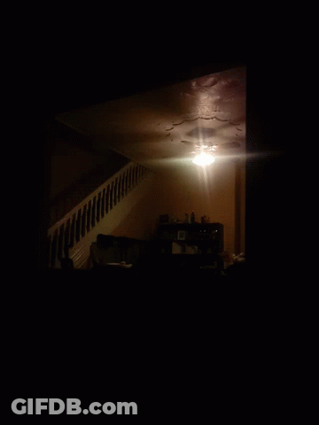A Dark Room With A Staircase Leading Up To A Shelf With Pictures On It GIF