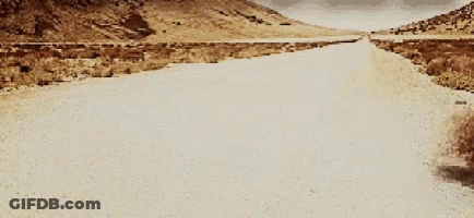 A Desert Road With Mountains In The Background GIF