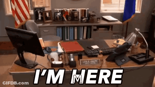 A Desk With A Computer And A Sign That Says I 'M Here On It GIF