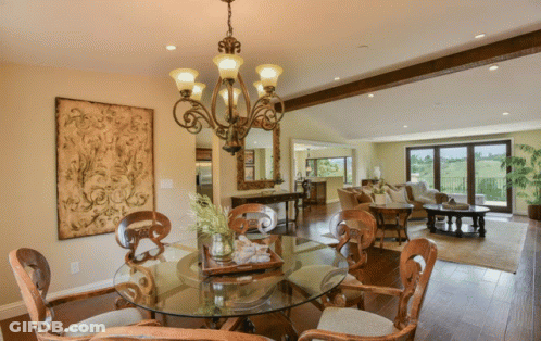 A Dining Room With A Round Glass Table And Chairs And A Chandelier GIF