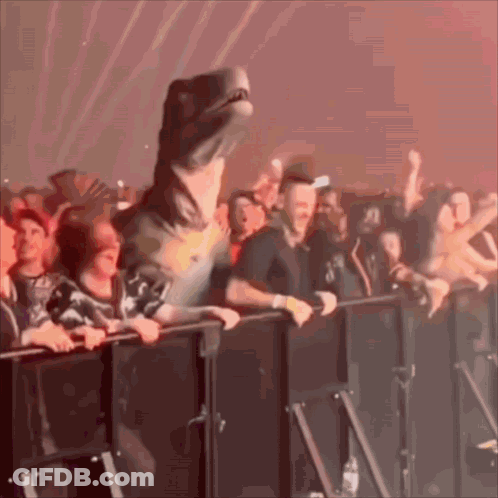 A Dinosaur Is Standing In Front Of A Crowd At A Concert . GIF