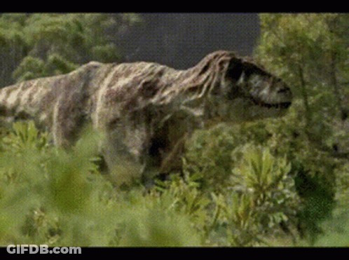 A Dinosaur Is Walking Through A Field Of Grass GIF