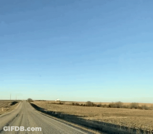 A Dirt Road Going Through A Field With A Blue Sky Behind It GIF