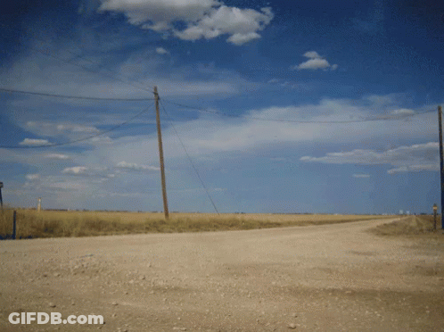 A Dirt Road Going Through A Field With Telephone Poles GIF