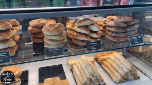 A Display Case Filled With A Variety Of Breads And Pastries With The Words Knead To Bake On The Bottom GIF