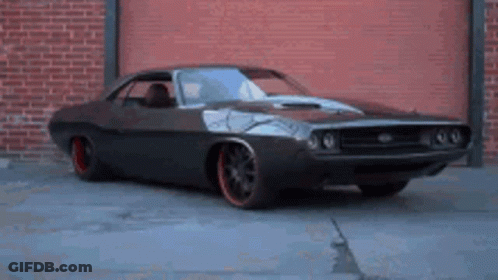 A Dodge Challenger Is Parked In Front Of A Brick Building GIF