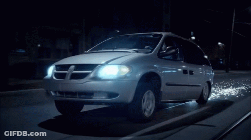 A Dodge Minivan Is Driving Down A Dark Street At Night GIF