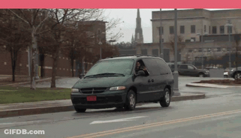 A Dodge Minivan Is Driving Down A Street With A Red License Plate That Says Rnm828 GIF