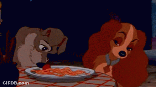 A Dog And A Woman Are Sitting At A Table Eating Spaghetti . GIF