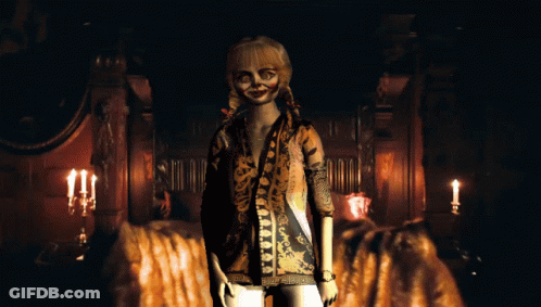 A Doll In A Leopard Print Shirt Stands In A Dark Room With Candles GIF