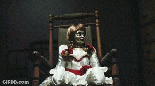 A Doll Is Sitting In A Chair With A Red Bow Around Her Neck GIF