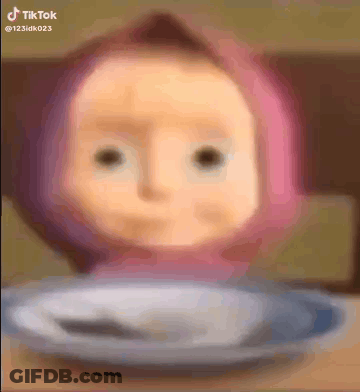 A Doll With A Pink Hat Is Sitting On A Plate With A Spoon . GIF