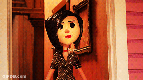 A Doll With Black Hair And Red Lips Stands In Front Of A Pink House GIF