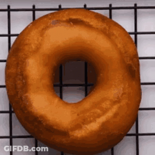 A Donut Is Sitting On A Wire Rack On A Table . GIF