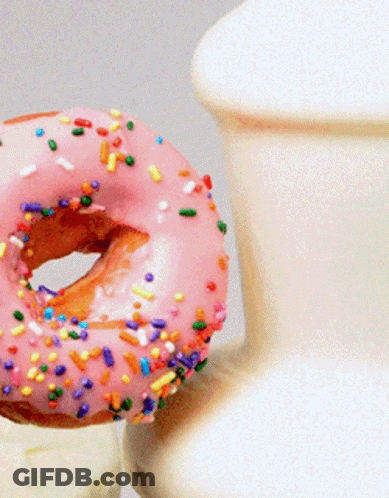 A Donut With Pink Frosting And Sprinkles Next To A Vase GIF